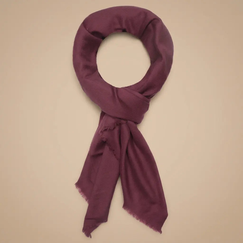 Burgundy cashmere scarf with fringed edges arranged on a warm beige background