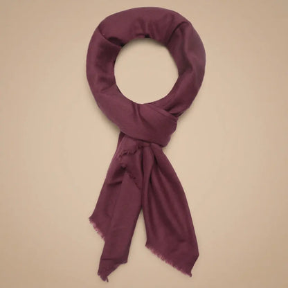 Burgundy cashmere scarf with fringed edges arranged on a warm beige background