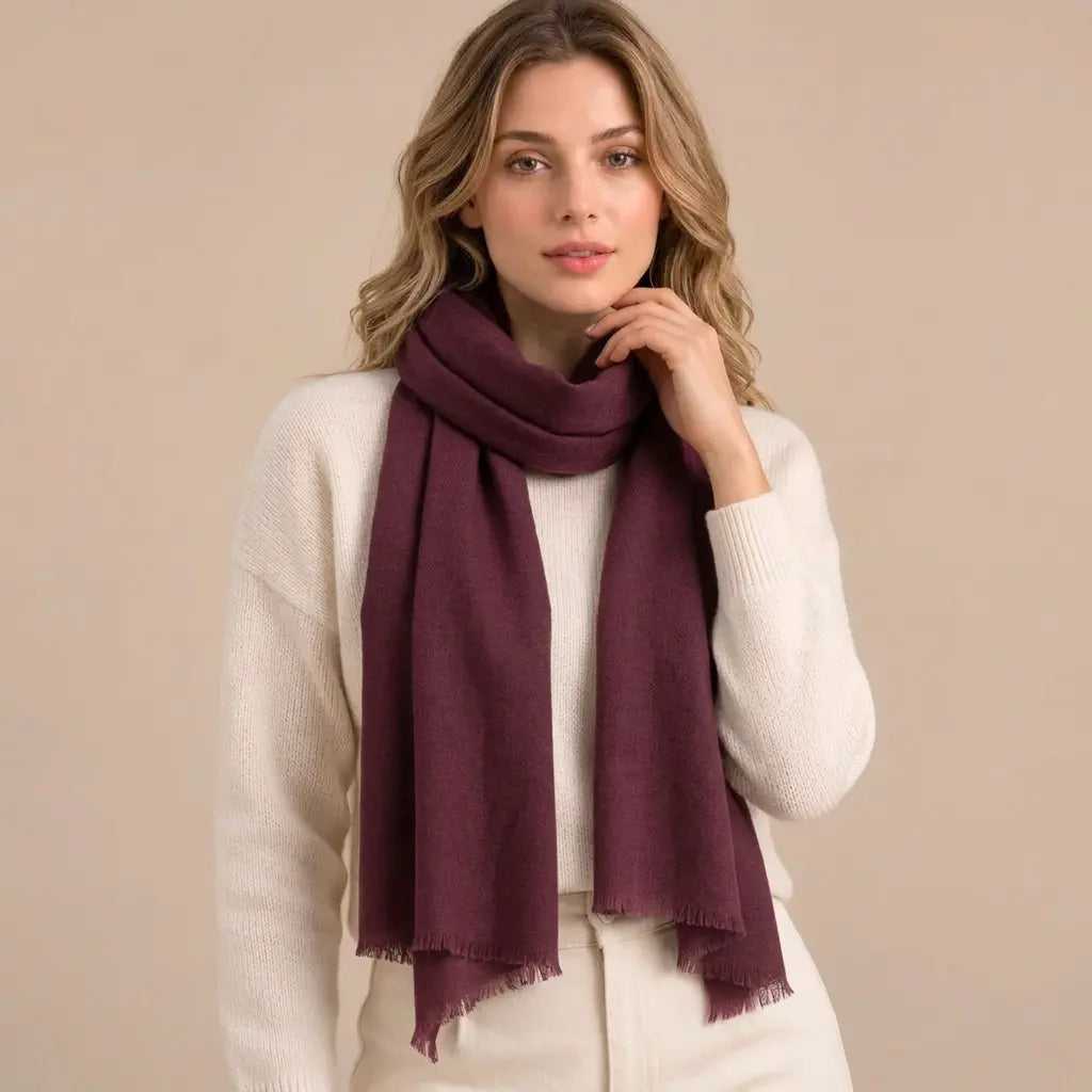 Model wearing a burgundy cashmere scarf with an ivory jumper against a warm beige studio background